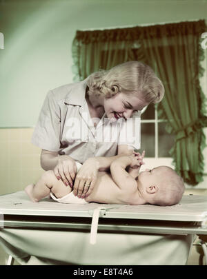 1950ER JAHRE BLONDE FRAU MUTTER WICKELN BABY MIT STOFFWINDEL Stockfoto