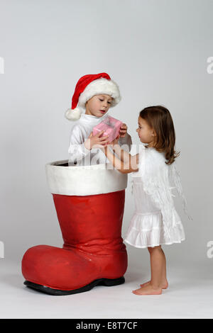 Junge in einem Weihnachts-Boot Übergabe ein kleines Weihnachtsgeschenk an einer Mädchen gekleidet wie ein Engel Stockfoto