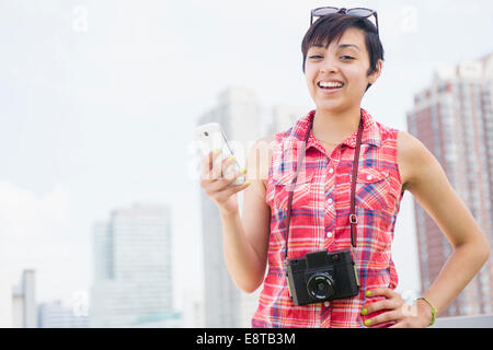 Gemischte Rassen Frau mit Kamera und Handy-lächelnd in der Nähe von Skyline der Stadt Stockfoto