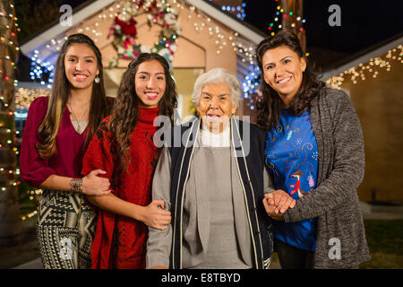 Drei Generationen von Hispanic Frauen Lächeln vor Haus mit Lichterketten dekoriert Stockfoto