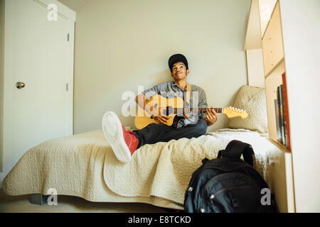 Gemischte Rassen junge spielt Gitarre im Schlafzimmer Stockfoto