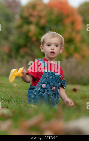 Ein zwei-Jahr-alte junge in einem roten T-shirt und Jeans Overall sucht in Überraschung während des Spielens in seinem Hof im Herbst. Stockfoto