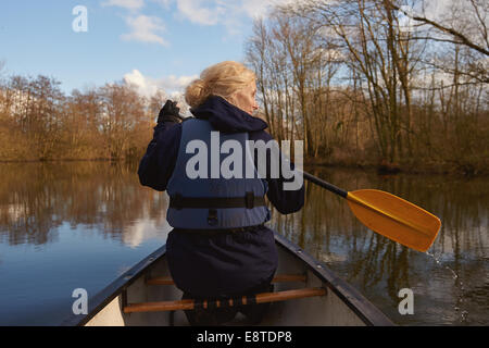 Eine Frau in den 30er Paddeln in einem Kanu entlang eines Flusses auf der Norfolk Broads Stockfoto