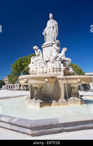 Blick auf Brunnen im Zentrum, Nimes, mit Amphitheater und Arena im Hintergrund, vor blauem Himmel Stockfoto