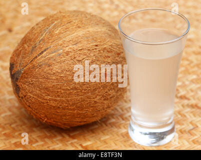 Frische Kokosnuss mit Wasser in einem Glas auf strukturierte Oberfläche Stockfoto