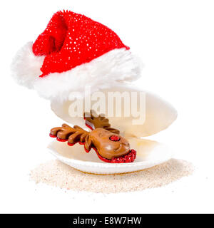 tropische Konzept von Weihnachten mit Shell, Schokolade Rentier und roten Weihnachtsmann-Mützen auf Sand isoliert, weißer Hintergrund Stockfoto