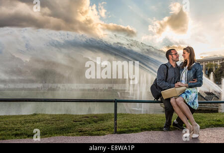 Junges Paar sitzt auf einem Zaun vor schönen Brunnen in der Abenddämmerung in Paris Stockfoto