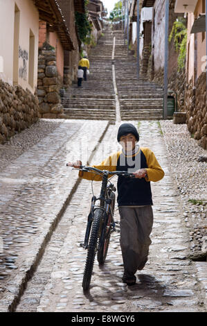 Ein Kind auf dem Fahrrad in einer der die steilen Straßen von dem kleinen Dorf Chinchero im Heiligen Tal in der Nähe von Cuzco. Chinchero ist Stockfoto