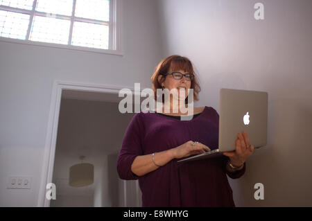 Eine Frau mittleren Alters mit ihrem Laptop in ihrem Haus Stockfoto