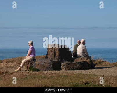 Menschen saßen auf einer öffentlichen Bank hergestellt aus großen Steinen entlang der südwestlichen Küstenweg Widemouth Bay, Bude, Cornwall, UK Stockfoto