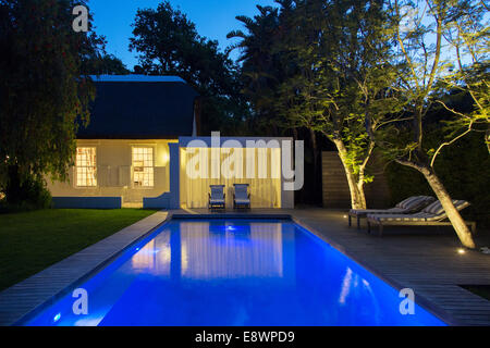 Gartenmöbel auf Holzterrasse durch beleuchtete Schwimmbad bei Nacht Stockfoto