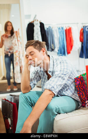 Gelangweilt Mann mit Freundin im Bekleidungsgeschäft einkaufen Stockfoto