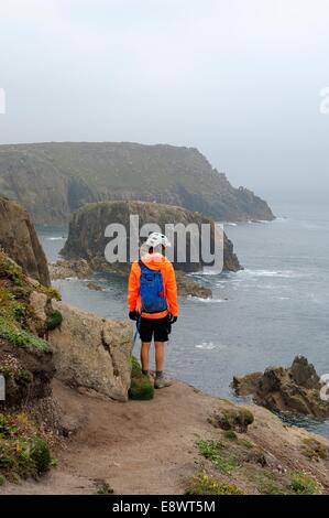 Ein einsamer weibliche Wanderer auf der Suche über die Felskante bei Lands End Cornwall UK Stockfoto