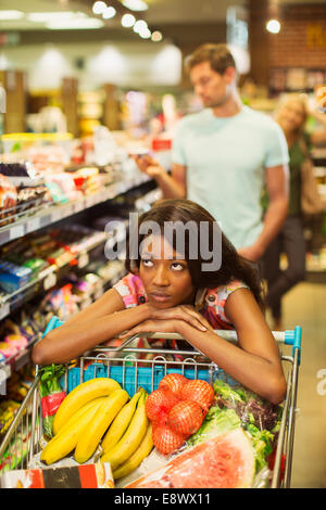 Gelangweilte Frau schob vollen Einkaufswagen im Supermarkt Stockfoto