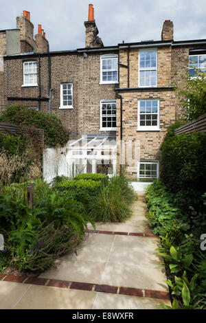 York Stein gepflasterten Weg, dazwischen mit roten Ziegeln, mit beschnittenen Box, Ziergräser, Akanthus und Alchemilla Mollis. Rückansicht von Haus und Garten in Greenwich, South East London, UK, entworfen von Modular Stockfoto