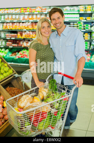 Paar lächelnd mit vollen Einkaufswagen im Supermarkt Stockfoto