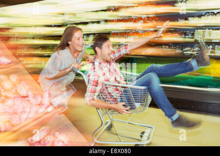 Verschwommene Sicht des Paares spielen mit Einkaufswagen im Supermarkt Stockfoto