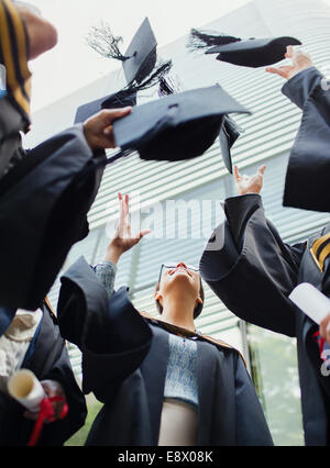 Studenten in Kleidern, die Mützen in die Luft werfen Stockfoto