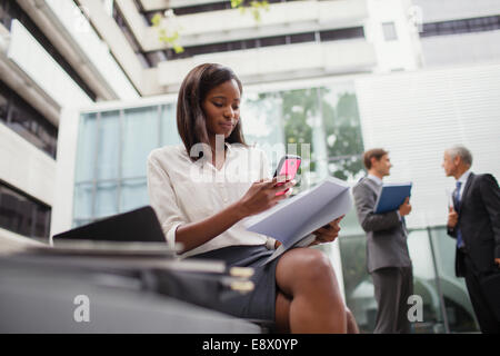 Geschäftsfrau, die sitzen auf Bank mit Handy außerhalb Stockfoto