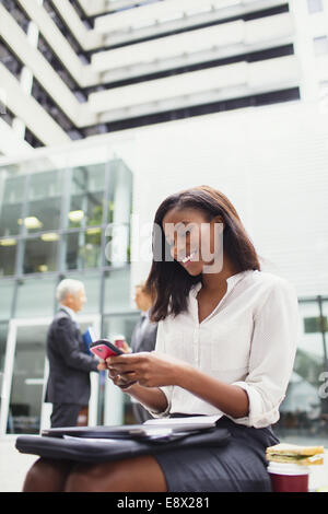 Geschäftsfrau, die sitzen auf Bank mit Handy außerhalb Stockfoto
