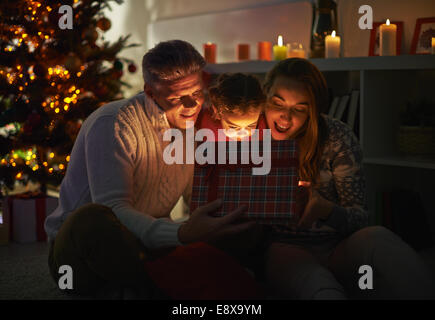 Glückliche Familie von drei Blick in offene Geschenkbox in der Weihnachtsnacht Stockfoto