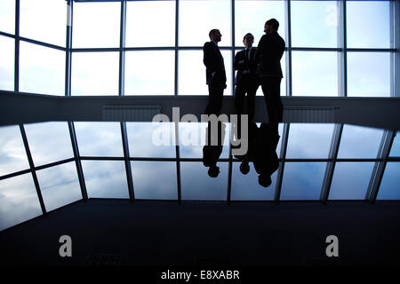Drei Geschäftspartner mit einer Diskussion stehende gegen ein Panoramafenster im Büro Stockfoto