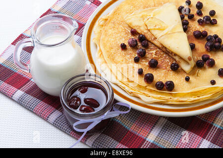 Frisch gebackene hausgemachte Pfannkuchen mit Beeren auf einer karierten Tischdecke und einen Krug Milch Stockfoto