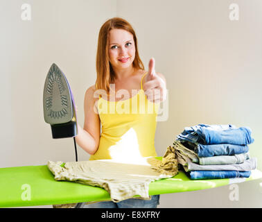 Junge schöne Frau, ein Bügeleisen/-Brett Kleidung im Zimmer auf grauem Hintergrund Stockfoto