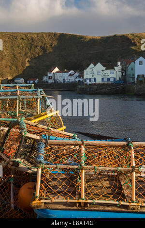 Sunlit Hummer Töpfe in einem Haufen gestapelt, mit Hafen, Gebäude & hohe Klippen hinaus - Fischerdorf Staithes, North Yorkshire, England. Stockfoto