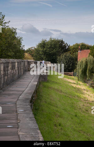 Zwei Personen, die gemeinsam auf einem malerischen historischen Gehweg auf einer sonnendurchfluteten mittelalterlichen Stadtmauer von York (alte Stadtmauer und Brüstung) spazieren - North Yorkshire, England, Großbritannien. Stockfoto