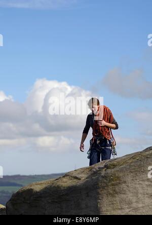 Eine junge Frau Kletterer mit Seilen über die Schulter zu Fuß entlang der Oberseite der Kuh und Kalb Felsen auf Moor, Ilkley, West Yorkshire Stockfoto