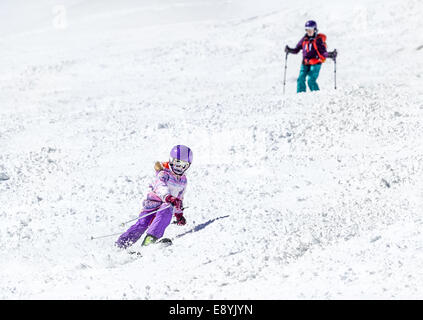 Kleines Mädchen auf den Skiern im weichen Schnee unter der Obhut meiner Mutter an einem sonnigen Tag in den Bergen Stockfoto