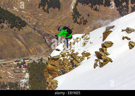 Frau Skifahrer springen über eine Klippe in den Bergen an einem sonnigen Tag auf Grund des Tals ohne Schnee Stockfoto