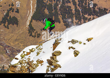 Frau Skifahrer springen über eine Klippe in den Bergen an einem sonnigen Tag auf Grund des Tals ohne Schnee Stockfoto