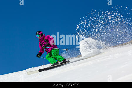 Skifahrer am Berghang auf einem klaren blauen Himmel. Im Gegenzug wirft den Schnee Staub. Stockfoto