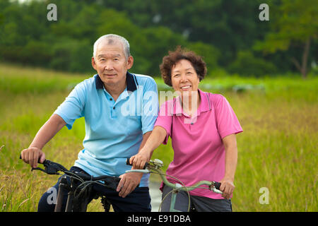 Glücklich asiatischen Senioren paar Radfahren im Park. Rente und Gesundheit-Konzept