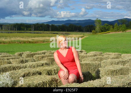 Schöne Frau im roten Kleid sitzt auf dem Heu Stockfoto