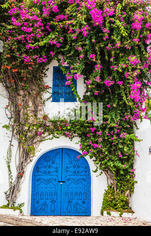 Eine typische blau, beschlagene Holztür mit Bougainvillea weiß getünchte Wand und Schmiedeeisen Schaufensterdekoration in Sidi aufwachsen Stockfoto