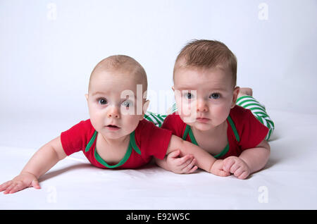 9 Monate altes zweieiige Zwillinge Jungs tragen Weihnachtsfarben, Hand in Hand und ernst Stockfoto