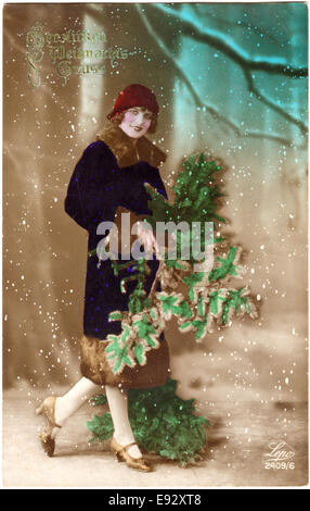 Lächelnde Frau in roten Hut und Blue Coat mit grünen Zweigen, handkolorierten Weihnachts Postkarte, ca. 1920 Stockfoto