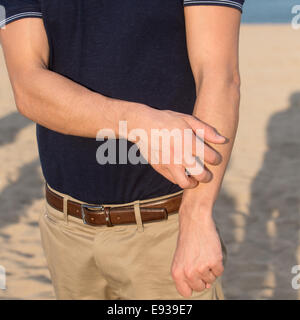Mann reibt Arm am Strand Stockfoto