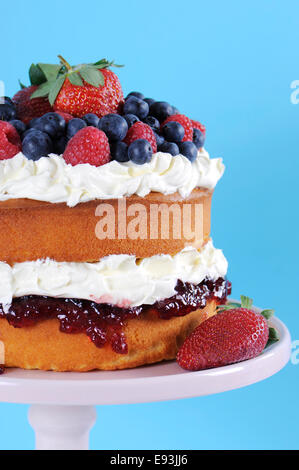 Frische Sahne und Beeren Schicht Biskuit auf Rosa Kuchen stehen gegen blassen blauen und weißen Hintergrund. Vertikale. Stockfoto