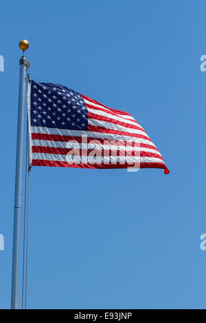 Ein Gewebematerial amerikanische Flagge flattert Wellen im Wind an einem klaren, blauen Himmel Tag. Viele textfreiraum geblieben. Stockfoto