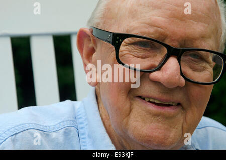 Porträt von ein älterer Herr in einem weißen Schaukelstuhl hautnah. Thema ist Lächeln auf den Lippen und auf der Suche von der Kamera entfernt.