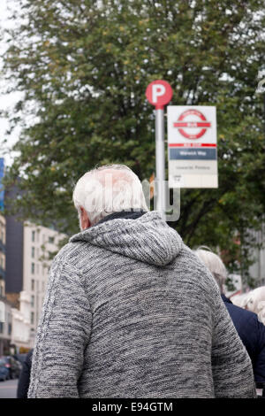 Ein älterer Herr in einem grauen Cardigan warten auf einen Bus auf Wilton Road, Pimlico, London, UK Stockfoto