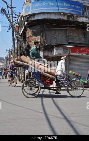 Ein Mann-Stämme in die Pedale treten ein Dreirad, schwer beladen mit Teppichen durch die Straßen von Delhi, während ein Junge an der Spitze reitet Stockfoto