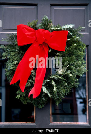 Ein großen hellen roten Urlaub Bogen befestigt um einen Kranz von Immergrün ziert die Eingangstür zu einem Haus in den USA in der Weihnachtszeit. Stockfoto