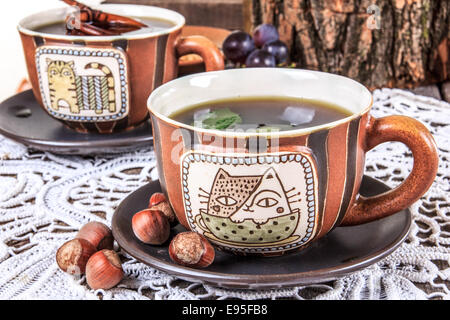 Tee Tasse Zusammensetzung am alten Holztisch mit Deckchen und Haselnüssen Stockfoto