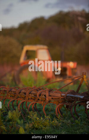 Ein Traktor und Fräse untätig in einem Feld bei Sonnenuntergang. Stockfoto