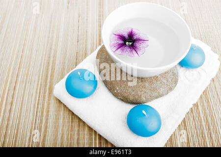Drei blaue Kerzen Handtuch und Blume Blütenblätter auf weiße Tasse gefüllt mit frischem klarem Wasser Spa und relax-Konzept mit selektiven Fokus Stockfoto